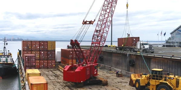 Image of large red crane on a barge unloading containers and equipment at Port MacKenzie Alaska